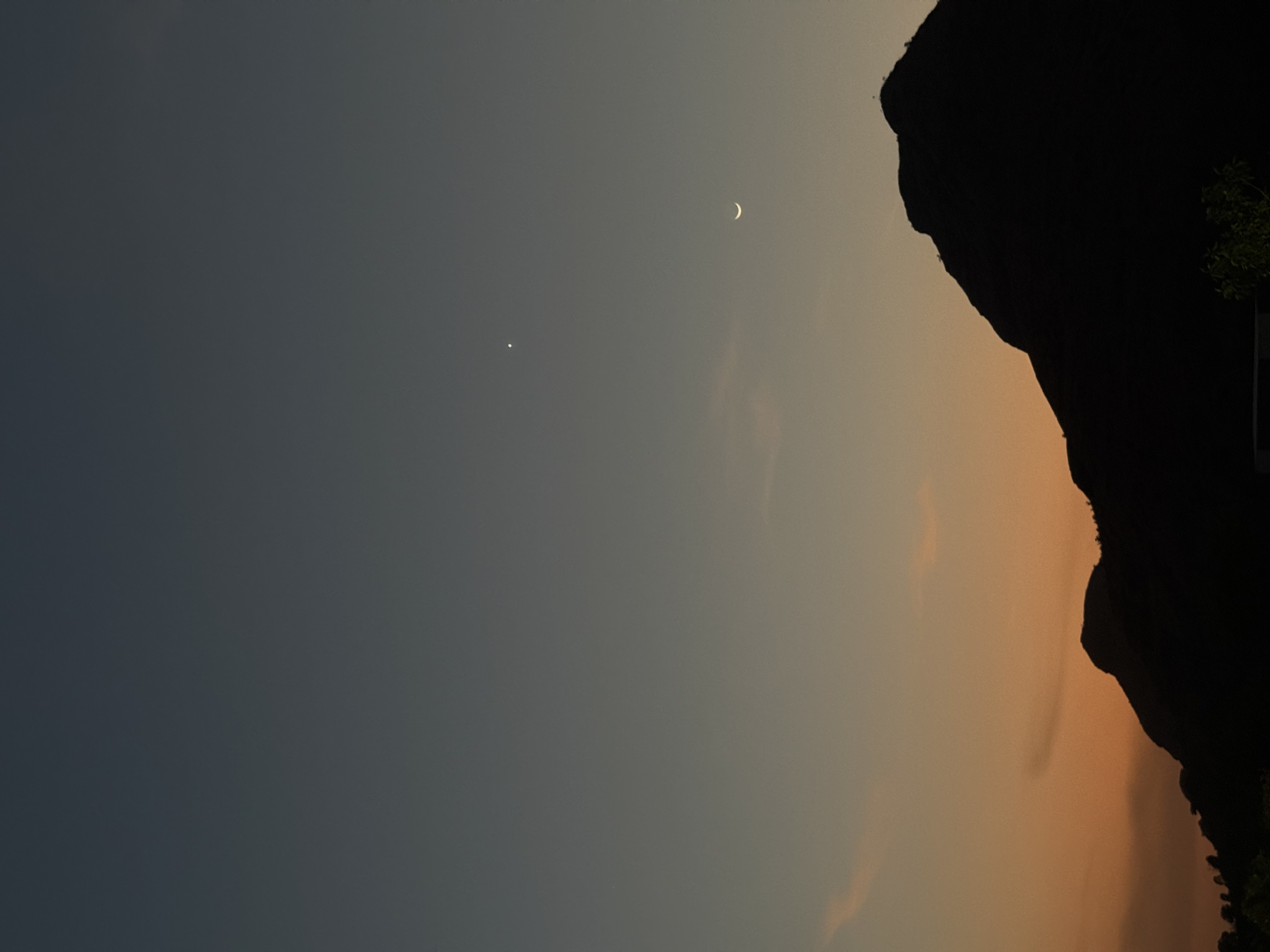 Crescent moon and a lone star above a mountain silhouette at dusk